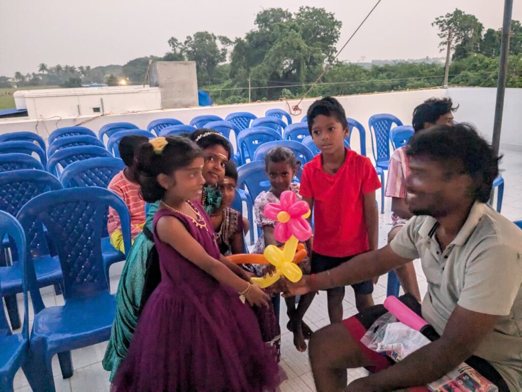 Balloon artist handing balloon flower designs to children at the birthday event in Tindivanam.

