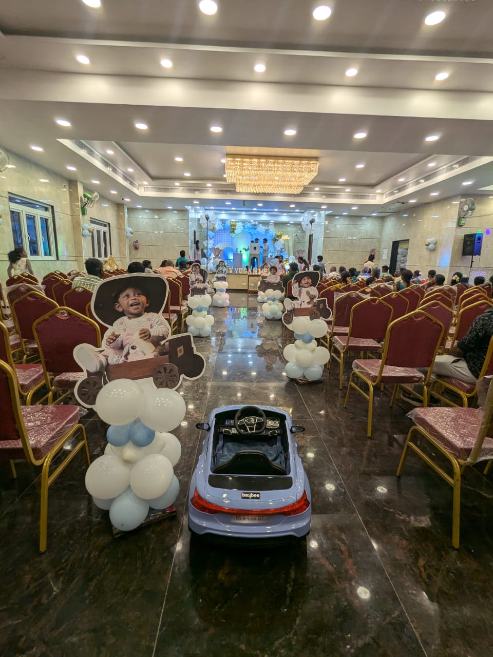 Hall birthday decoration with balloon pillars, child cut-outs, toy car pathway setup, and premium stage backdrop, priced at ₹27,000.