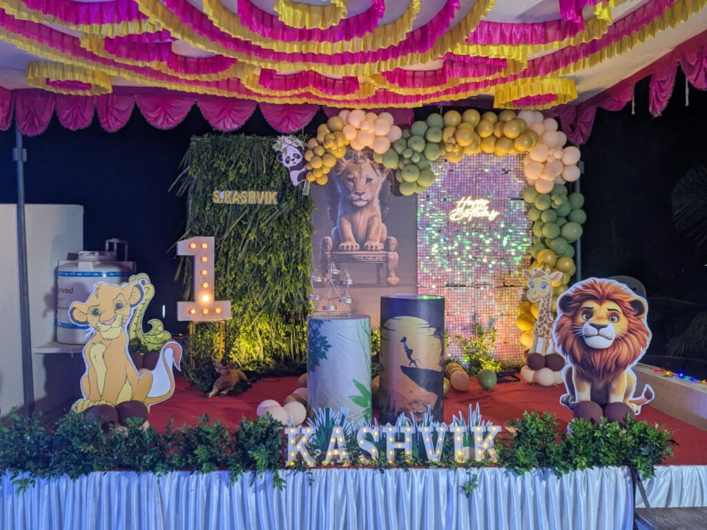  Full view of Lion King themed birthday setup with jungle backdrop, balloon garland, pedestals, and LED name lights.
