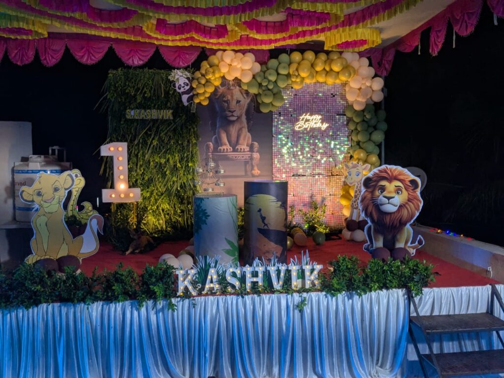 Jungle theme stage with Simba standee, giraffe decoration, balloon arch, and shimmer background.

