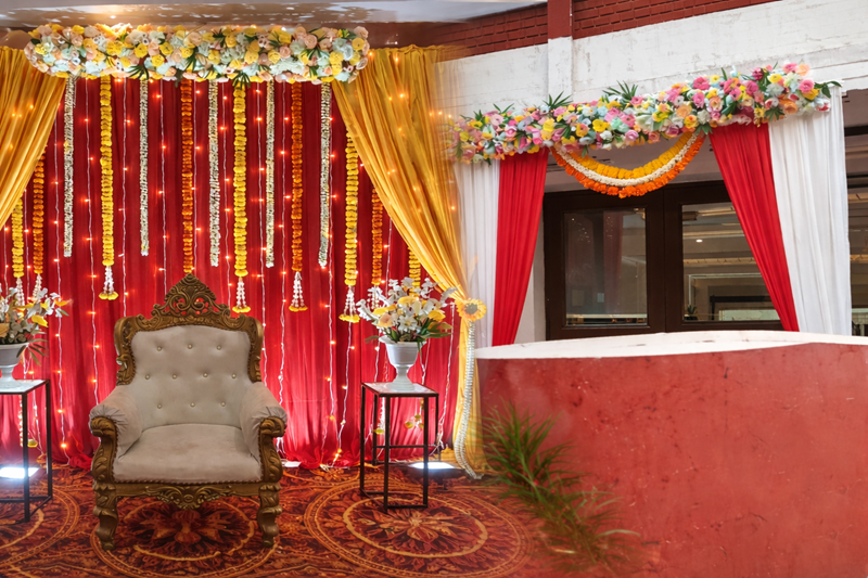 Simple Mehendi function stage decoration with red drapes, marigold garlands and royal chair at Madras Boat Club Chennai